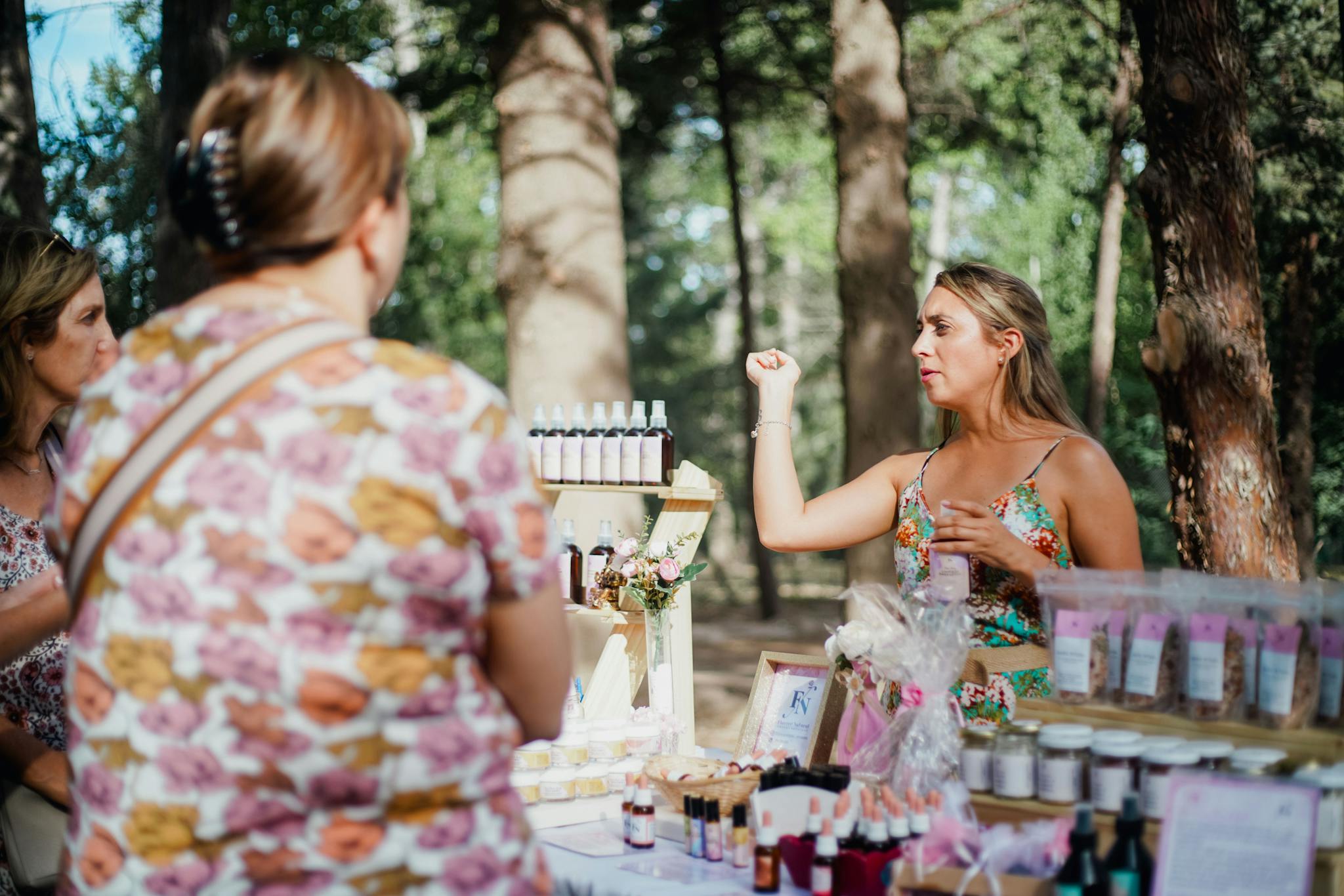 Women shopping at an outdoor market stall selling handmade cosmetics.